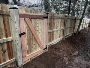 A newly installed wooden privacy fence with a custom gate in a wooded residential area by AFK FENCE LLC in Waldorf, MD.