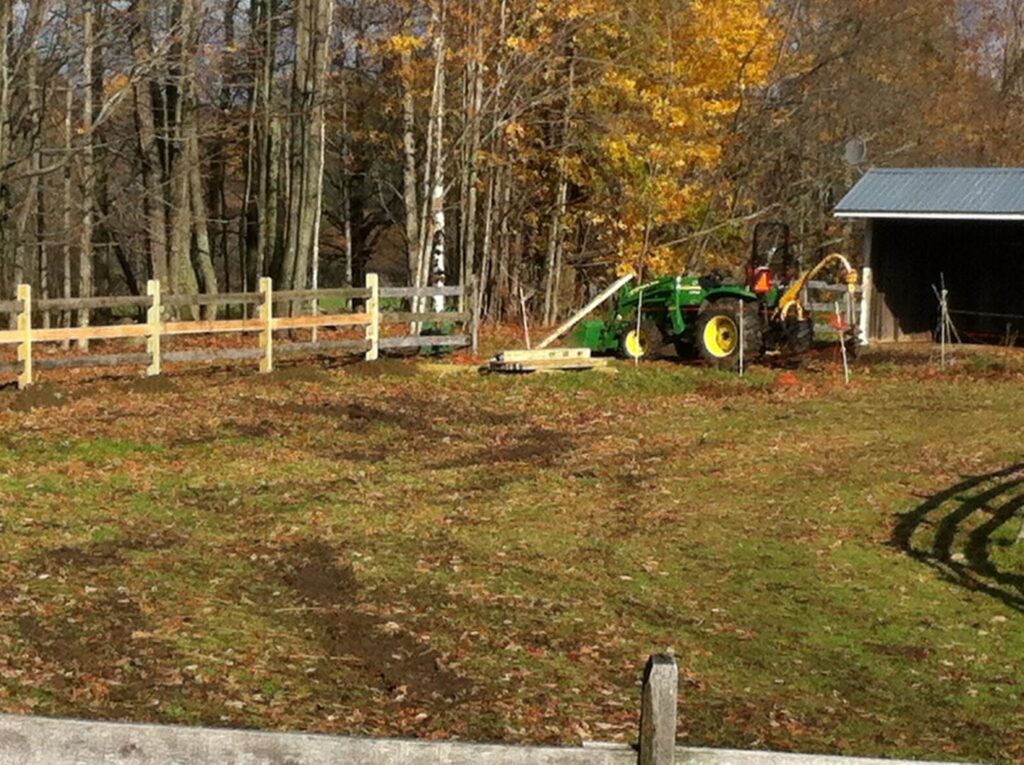 A wooden rail fence under construction with a tractor nearby, being built by Doolan Fence in Montpelier, VT.
