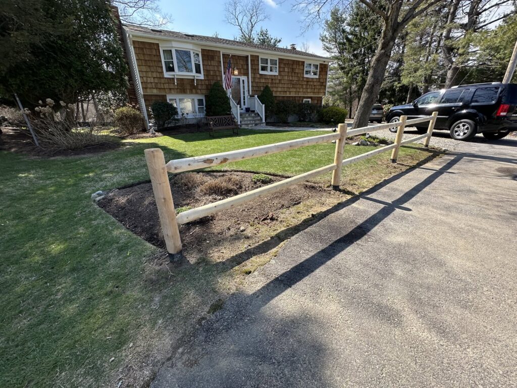 A newly installed wooden split-rail fence along a driveway by Fence Pros Direct in Saunderstown, RI.