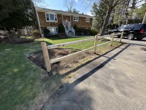 A newly installed wooden split-rail fence along a driveway by Fence Pros Direct in Saunderstown, RI.