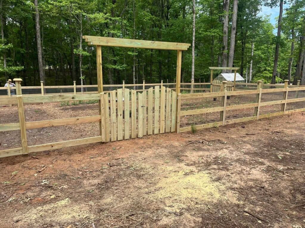 A wooden split rail fence with wire mesh and a gate with an arbor installed by JB Nealy Fence in Elgin, SC.