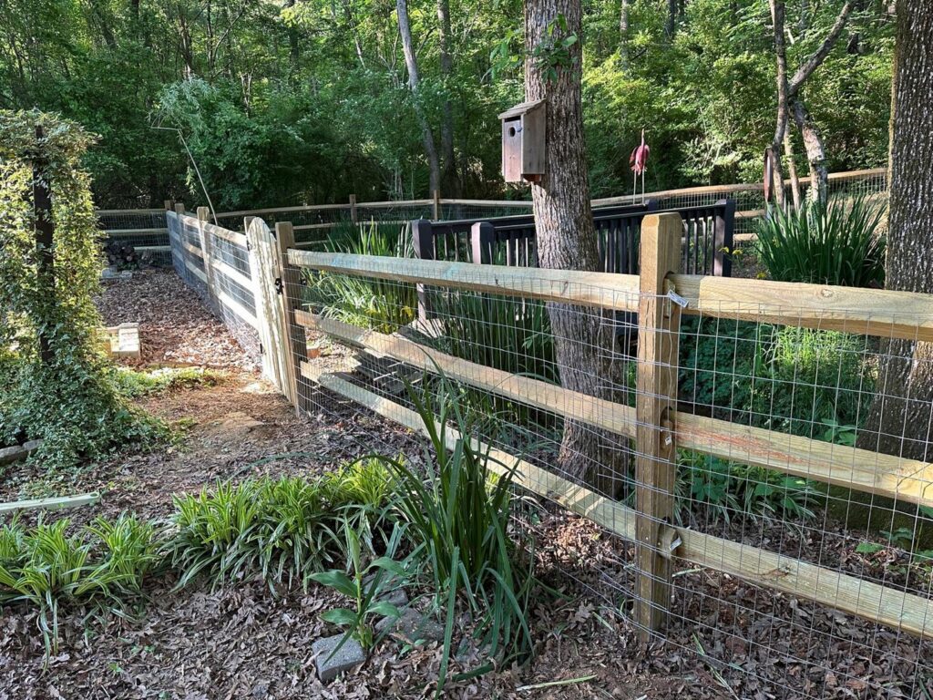 A wooden split rail fence with wire mesh and a gate installed in a wooded area by Sunrise Fences in Monroe, NC.