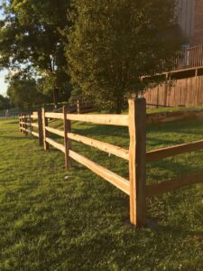A rustic wooden split rail fence installed along a green lawn by Roy & Son Fencing in Lee's Summit, MO.