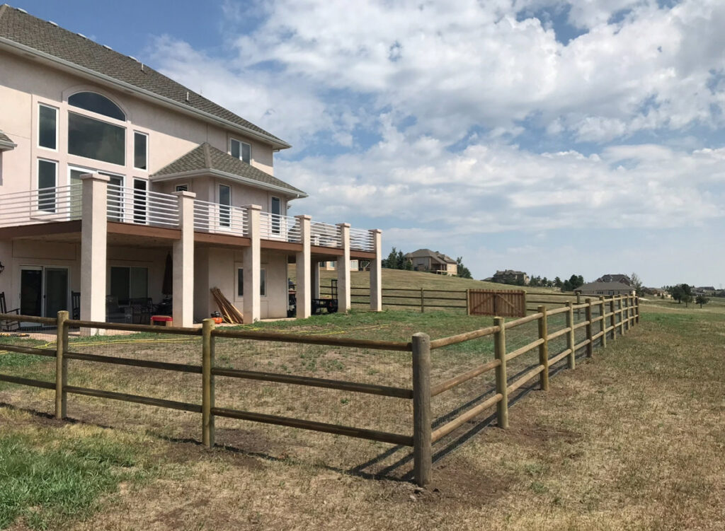 A wooden split-rail fence enclosing a large property with a house, installed by Colorado Springs Fence Company in Colorado Springs, CO.