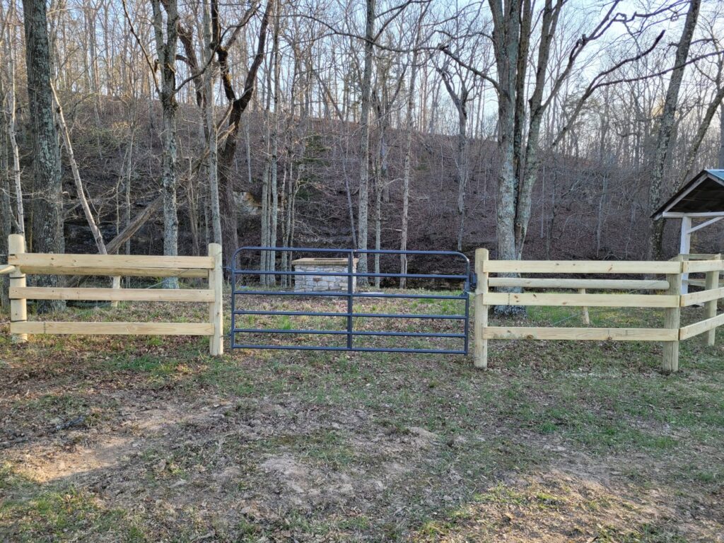 Wooden split-rail fence with a metal gate installed by National Fence and Gate in Ironton, MO, in a wooded area.