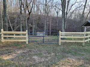 Wooden split-rail fence with a metal gate installed by National Fence and Gate in Ironton, MO, in a wooded area.