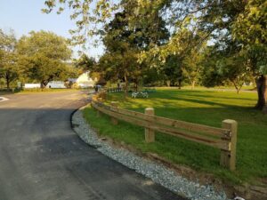 A wooden split-rail fence installed along a paved path in a park by 802 Fence Company LLC in Shoreham, VT.