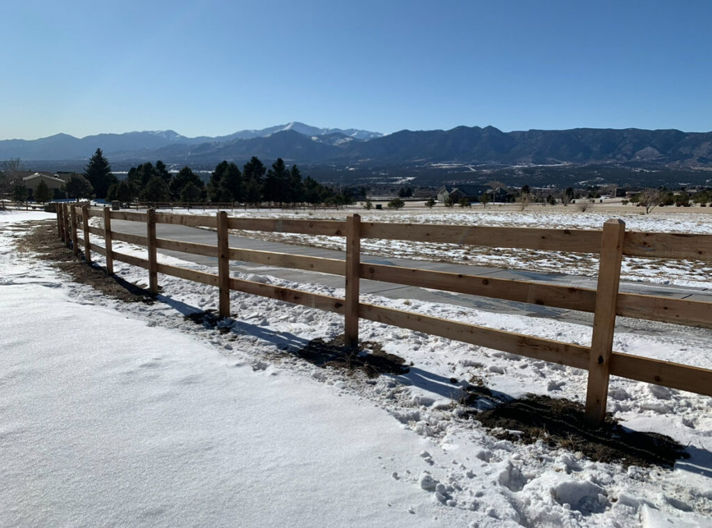A wooden split-rail fence in a snowy landscape with mountains, installed by Colorado Springs Fence Company in Colorado Springs, CO.