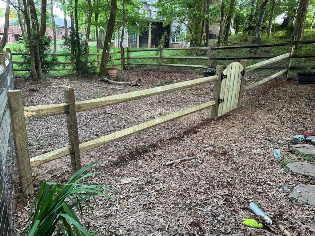 A wooden split rail fence with wire mesh and a gate installed in a wooded backyard by Sunrise Fences in Monroe, NC.