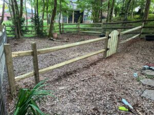 A wooden split rail fence with wire mesh and a gate installed in a wooded backyard by Sunrise Fences in Monroe, NC.