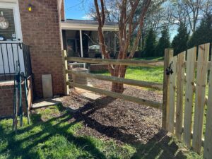 A wooden split rail fence with wire mesh and a gate installed next to a brick house by Sunrise Fences in Monroe, NC.