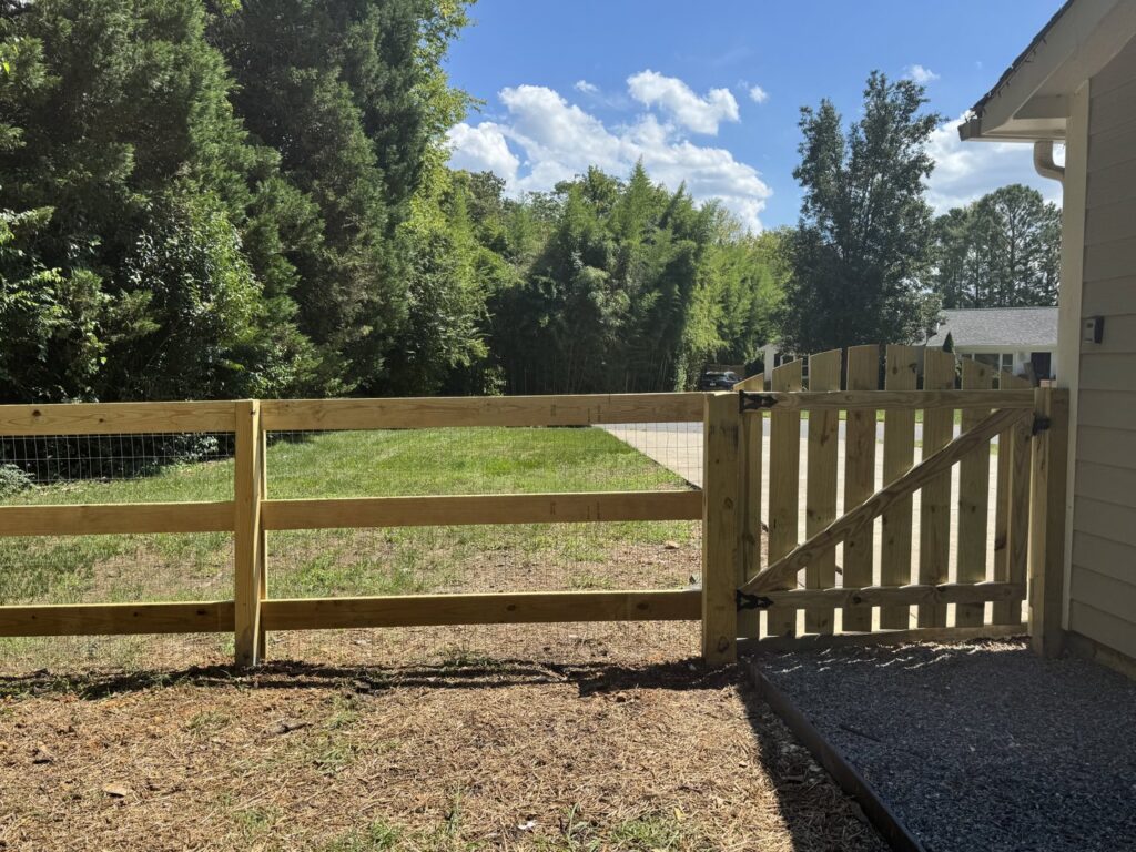 A new wooden split rail fence with wire mesh and a gate installed by Sunrise Fences in Monroe, NC.