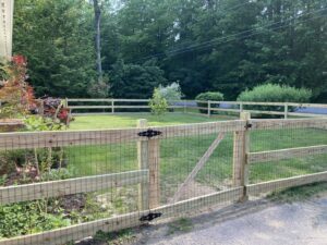 A wooden split-rail fence with wire mesh and a gate, installed in a green yard by Triple P Fence in Augusta, ME.