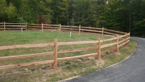 A long wooden split-rail fence with wire mesh installed along a curving driveway by 802 Fence Company LLC in Shoreham, VT.
