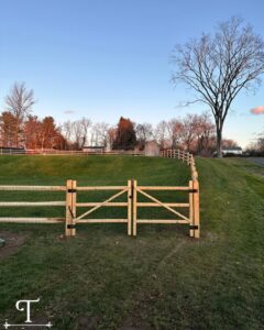A wooden split-rail fence with wire mesh and a gate, installed on a grassy hill by Teto's Fence Installation in Bridgeport, CT.