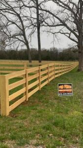A long wooden split-rail fence with a Pro Fence sign installed in a rural setting by Pro Fence in Decatur, AL