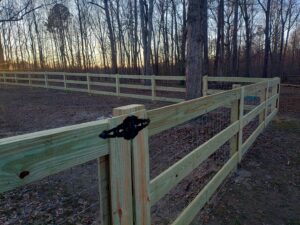 A newly installed wooden split-rail fence with wire mesh extending into a wooded area by Kelley Fence and Gate in Eva, AL.