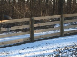 A sturdy wooden split rail fence with wire mesh, standing strong in a snowy landscape, built by Roark Fencing in Lexington, KY.