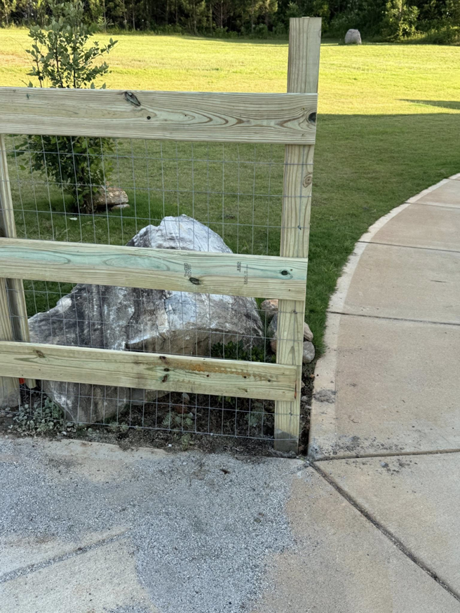 A custom wooden and wire mesh fence expertly installed around a large landscape rock by G2 Home Solutions in Phenix City, AL.