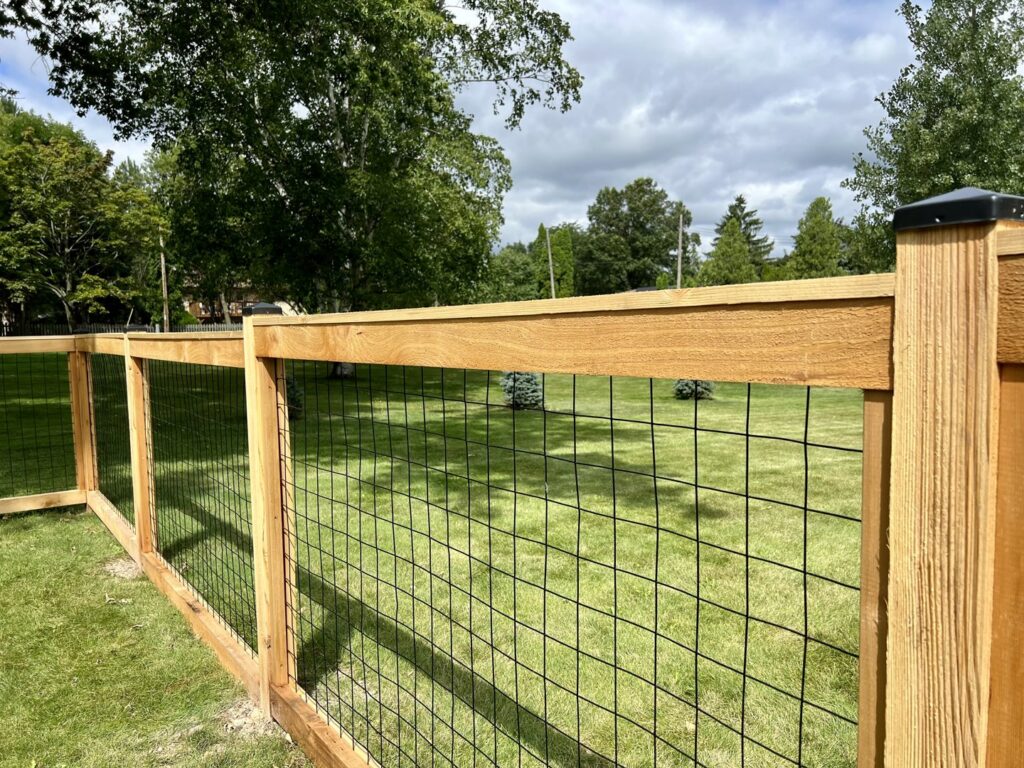 A new wooden fence with black wire mesh infill enclosing a spacious backyard by Chisel + Vine in Milwaukee, WI.