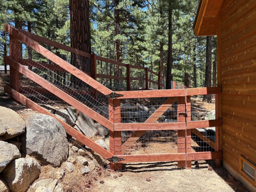 A rustic wooden fence with wire mesh and a gate in a natural, wooded setting by Finest Fence in Simi Valley, CA.