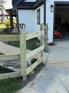 A custom wooden and wire mesh fence with a small gate installed next to a modern home by G2 Home Solutions in Phenix City, AL.