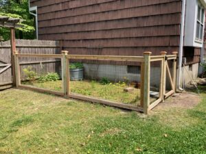 A custom wooden fence with wire mesh enclosing a garden area next to a home by MAC Fencing LLC in Toms River, NJ
