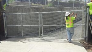 A worker in a hard hat and safety vest adjusting a chain-link gate for David's Fencing Inc. in Waipahu, HI.