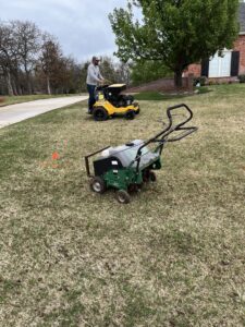A worker operating a lawn spreader for seeding or fertilizing, with an aerator in the foreground, by Perez Lawn Care llc in Oklahoma City, OK