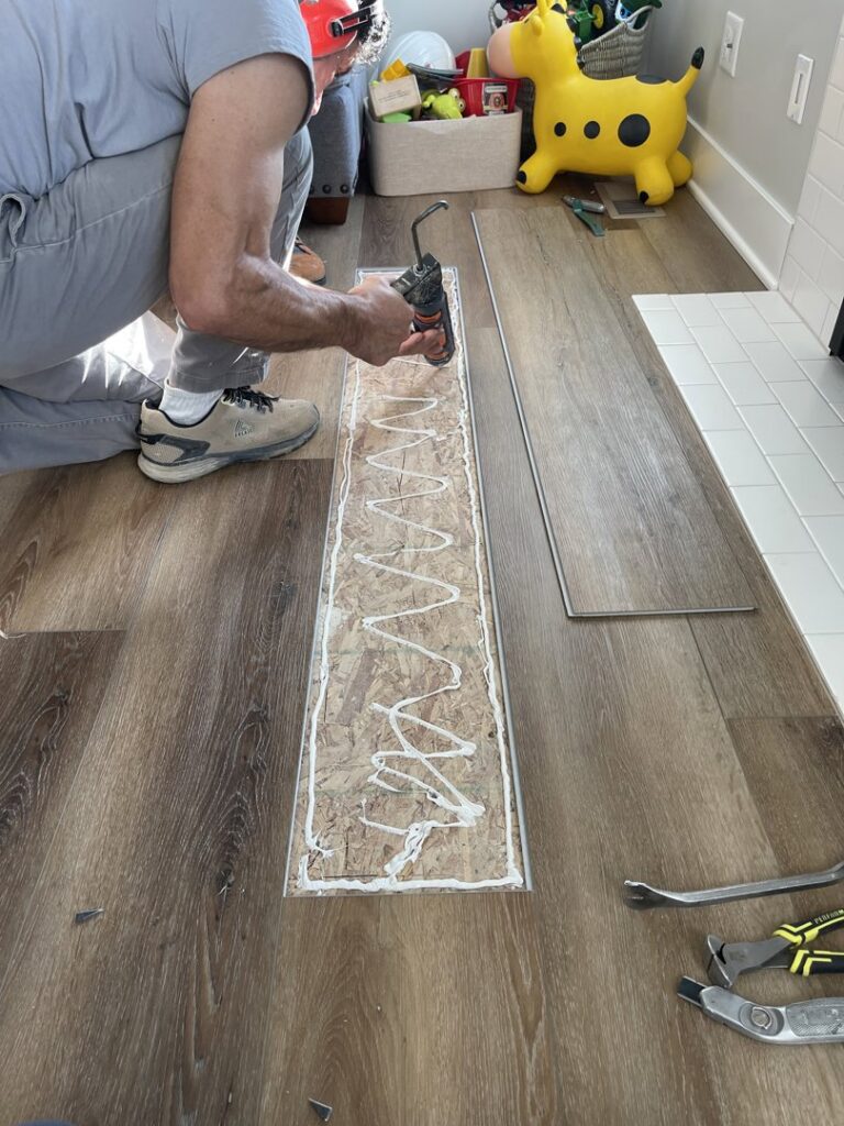 A worker applying adhesive for LVP flooring installation by Mendez Carpet in Grand Rapids, MI.