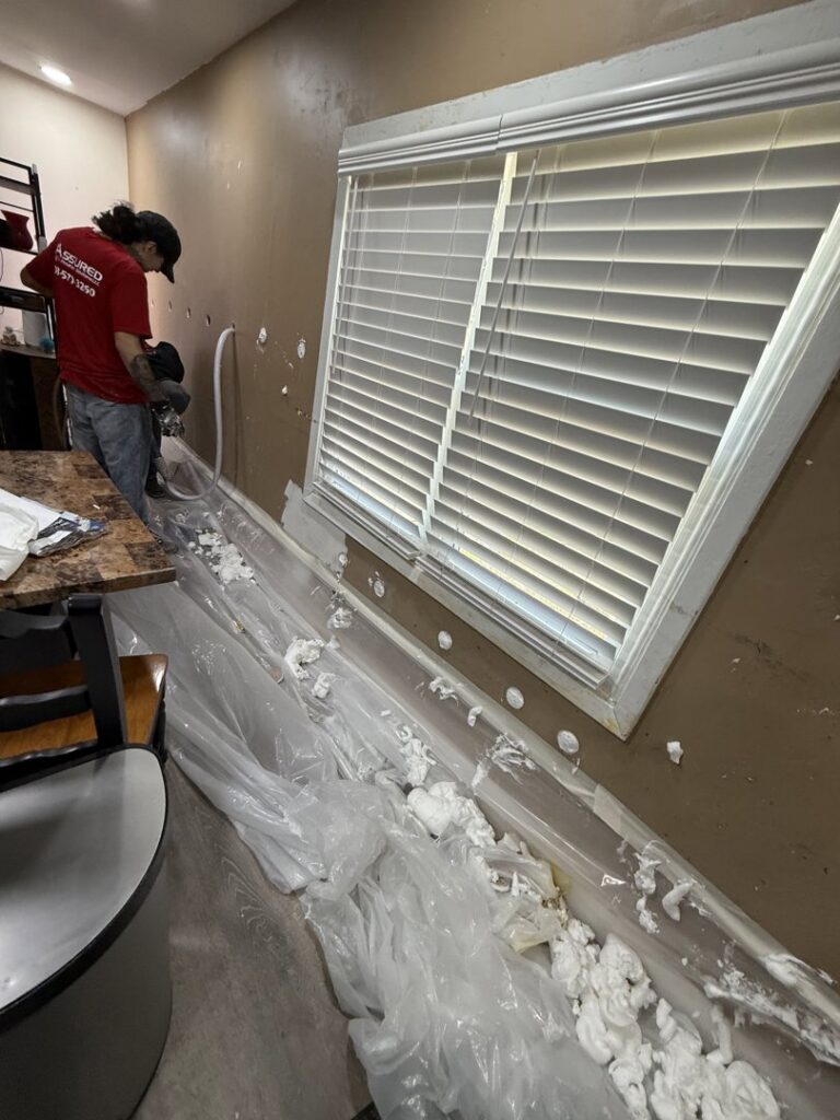 A worker applying spray foam insulation to a wall for Assured Energy Solutions in Frankfort, IL.