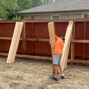 A worker carrying wooden fence pickets for installation by 2 Guys & A Girl Lawn Care in Thornton, CO.