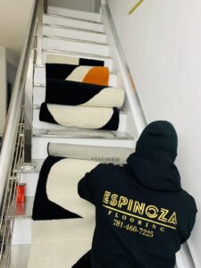 A worker from Espinoza Flooring Inc carrying rolled rugs up a staircase in Woburn, MA.