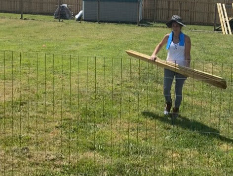 A worker carrying wooden fence rails across a grassy area for a project by Stapleton Fencing LLC in Lexington, KY.