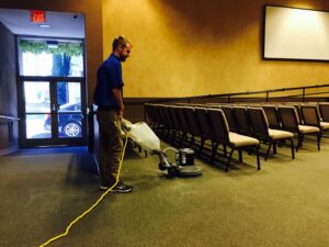 A worker cleaning a large carpeted area in an auditorium with a floor buffer for Spectrum Cleaning & Restoration in Medford, OR