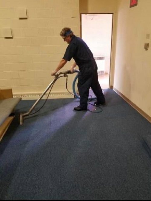 A worker professionally cleaning a blue carpet in a commercial hallway with a carpet cleaning machine for Pichey's Clean Rite in Flint, MI.