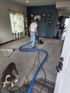A Clean-Master worker using a rotary machine to clean a residential carpet in Coeur d'Alene, ID, with hoses visible.