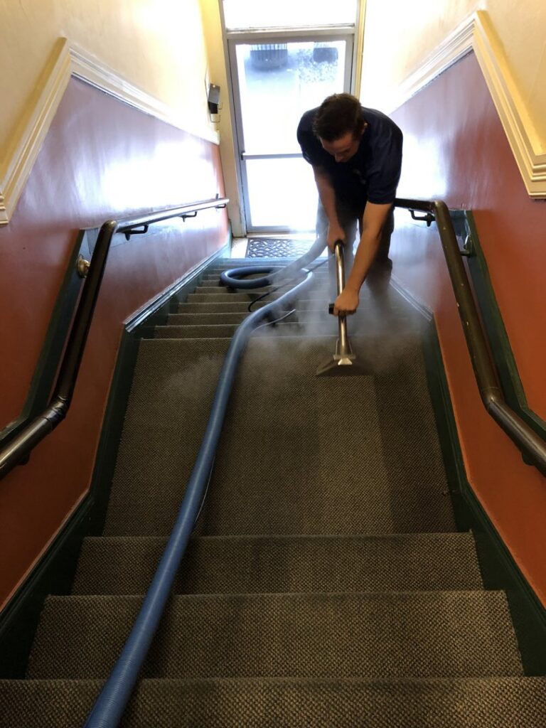 A worker professionally cleaning carpeted stairs with a steam cleaning wand for Spectrum Cleaning & Restoration in Medford, OR