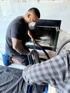 A worker in a mask using a specialized vacuum to clean a fireplace during a chimney sweep job by Ignite Chimney & Fireplace in Chicago, IL.