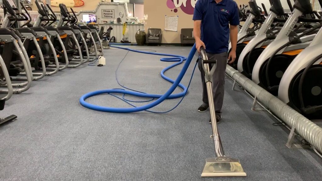 A worker cleaning a blue carpet in a gym with professional equipment for Spectrum Cleaning & Restoration in Medford, OR