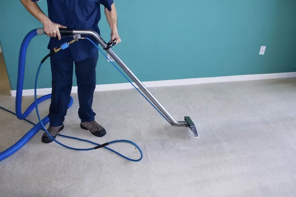 A worker performing carpet cleaning on a light-colored carpet with professional equipment for Pichey's Clean Rite in Flint, MI.