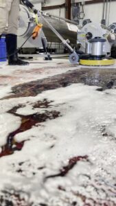 A worker using a floor buffer to clean a large area rug, with cleaning foam visible, at Advanced Cleaning Systems in Atlanta, GA.