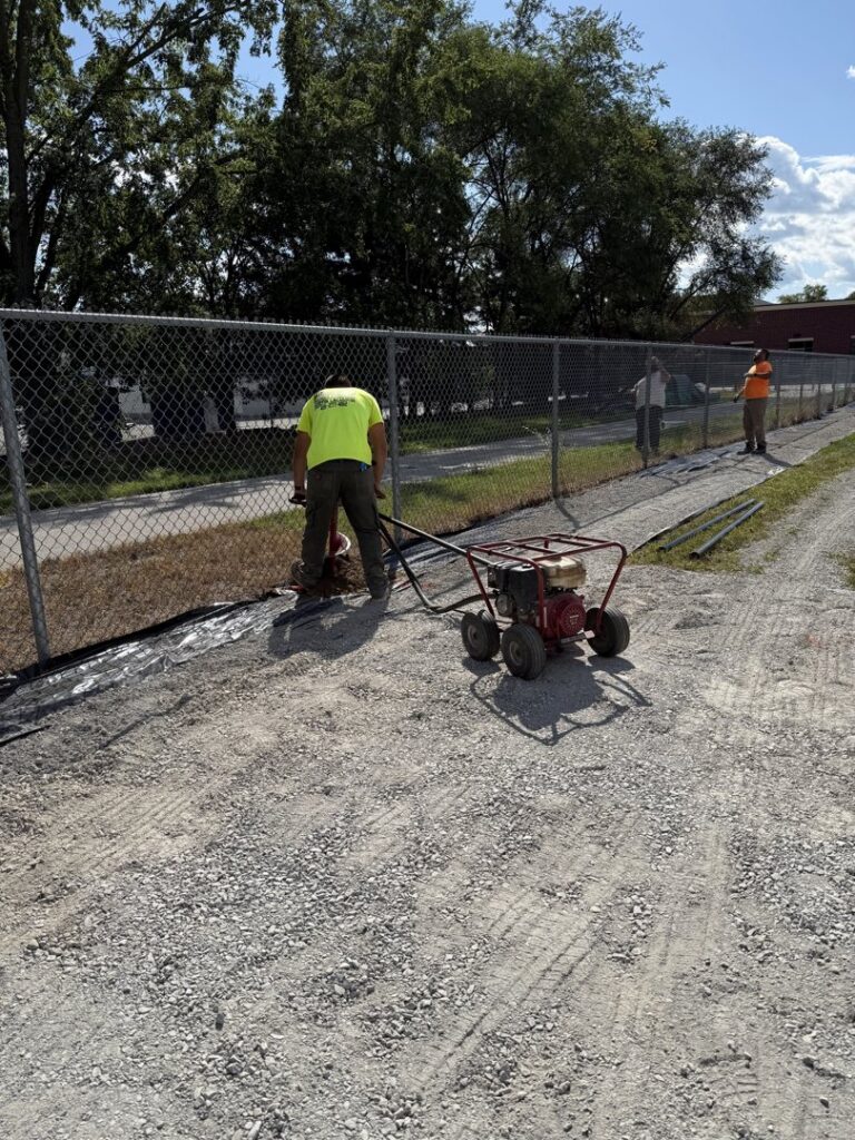 A worker compacting the ground next to a chain-link fence installation by Premier Fence LLC in Canton, MA.