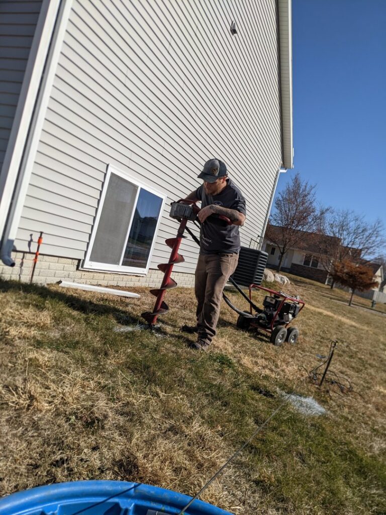 A fencing contractor worker using a power auger to dig post holes for a new fence installation by Corridor Residential Fencing Co. in Cedar Rapids, IA.
