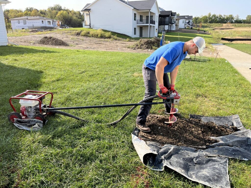A Thrive Fencing worker using a portable auger to efficiently dig a post hole for a new fence installation in Ames, IA.