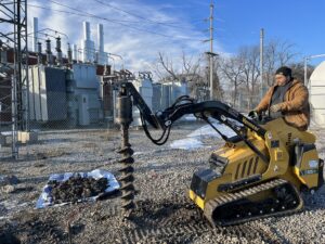 A Thrive Fencing worker operating a mini skid steer with an auger attachment to dig a post hole in Ames, IA.