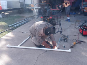 A worker fabricating metal fence or gate sections on the ground for Morin Fencing in Corpus Christi, TX.
