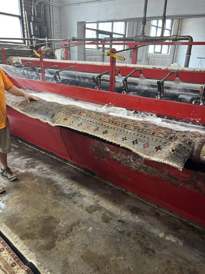 A worker guiding an oriental rug through an industrial cleaning machine at Harb's Carpeting & Oriental Rugs in Knoxville, TN