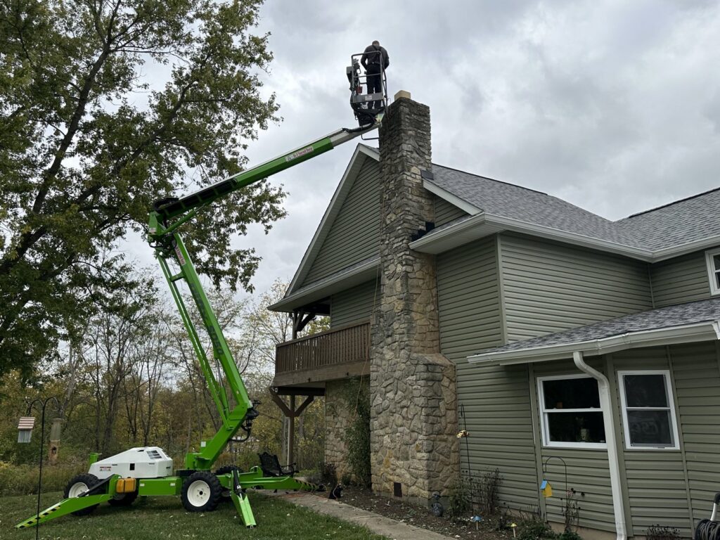 A worker in a boom lift performing chimney service on a house by Clean Sweep Chimney Service in Saint Charles, MO.