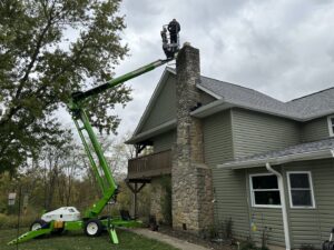 A worker in a boom lift performing chimney service on a house by Clean Sweep Chimney Service in Saint Charles, MO.